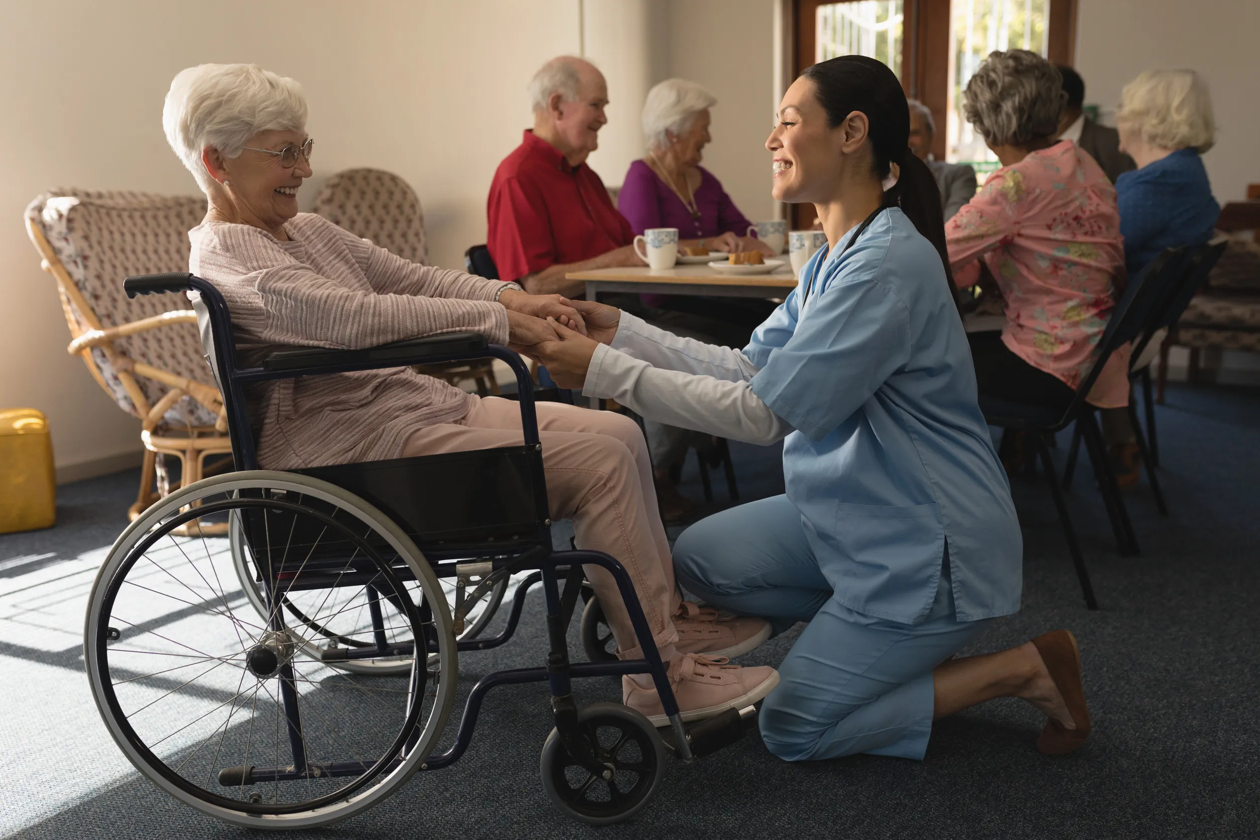Side view of happy female doctor holding hands and talking with disable senior woman at home Side view of happy female doctor holding hands and talking with disable senior woman at home